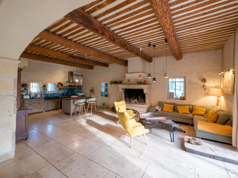 Salon lumineux avec des murs clairs, des poutres apparentes et des meubles confortables.